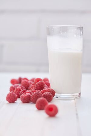 Glass of milk and raspberries are on white tableの写真素材