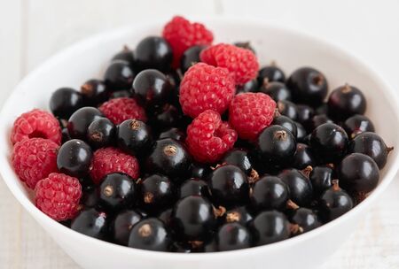 Ripe raspberries and currants are in white ceramic bowl.の写真素材