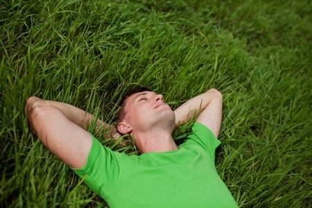 young man lying on the grass with his hands behind his headの写真素材