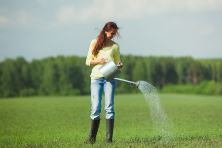 girl pours from a watering can on the grass fieldの写真素材