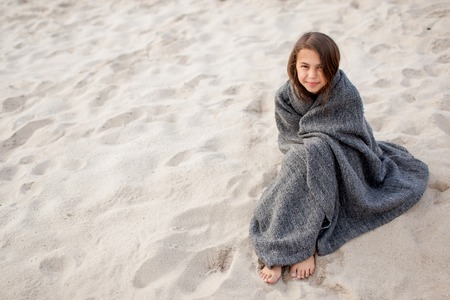 girl wrapped in a blanket on the sandの写真素材