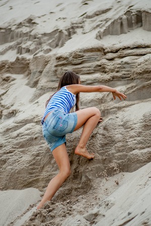 little girl climbing on the sand in a vestの写真素材