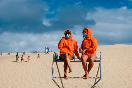 La Teste-de-Buch - 08/28/2020: two girls lifeguard with orange jackets and mask protection at Dune de Pyla beachのeditorial素材