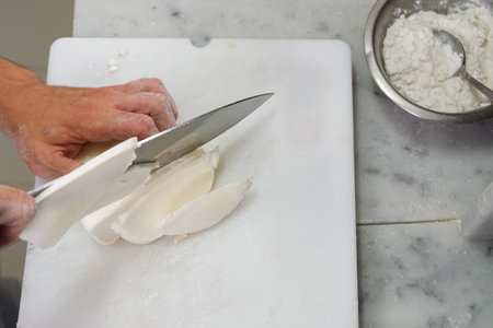 Chef cutting the dough on a white cutting board with a knifeの写真素材