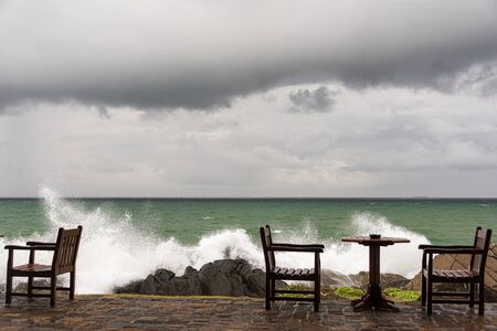 Galle, Sri Lanka, Sept 2015: Angry waves crash over rocks on the coast near abandoned tables and...