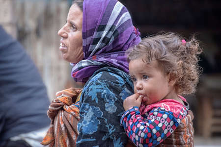 Essaouria, Morocco - September 2017: A homeless beggar woman walks through town with a young girl...