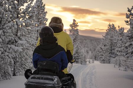 Finland, Inari - January 2019: 2 people riding on a snowmobile through the wilds of Lapland, under a red skyの写真素材