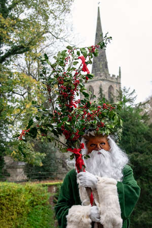 UK, Market Bosworth, Victorian Christmas Fair - December 2015: Father Christmas robed in green, masked and carrying holly branches, church tower in backgroundのeditorial素材