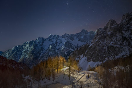 A welcoming wooden cottage illuminating mountain peaks, under a starry skyの写真素材
