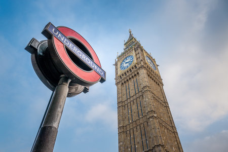 London Underground Sign and Big Ben Clock Tower Viewed from Below on a Clear Dayの写真素材