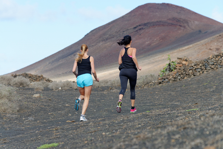 Two female running athletes. Women trail runner sprinting for success goals and healthy lifestyle in amazing nature landscape.の写真素材