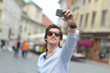 Young fashionable hipster Hispanic man with sunglasses taking a selfie on the city streetの写真素材
