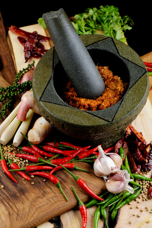 Asian herbs, spices and vegetables on the wooden plate with mortar making curry pasteの写真素材