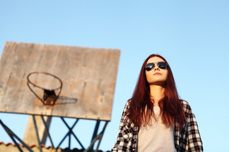 girl with sunglasses looking at the sky behind with old basketball hoopの写真素材