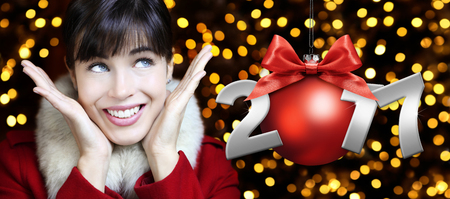 woman with Christmas red ball, smiling and looks up on lights