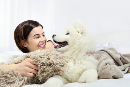 Smiling woman with pet dog lying in bedの写真素材