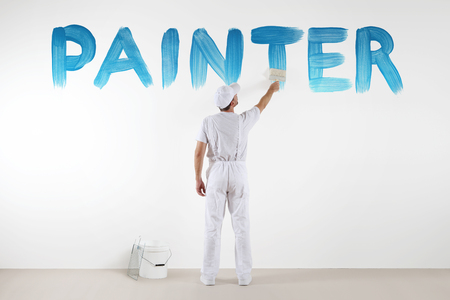 painter man with paint brush drawing a blue painter text isolated on the blank white wall.の写真素材