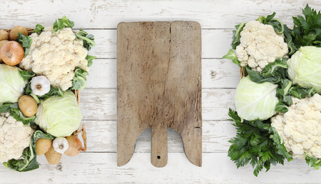 Healthy eating concept wooden cutting board with basket vegetables cabbage and cauliflower on kitchen white worktop, copy space, top view.の写真素材