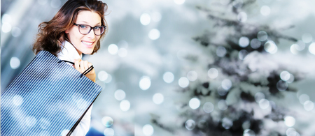 christmas shopping, smiling woman with bags on blurred bright lights background, banner template with copy space.の写真素材