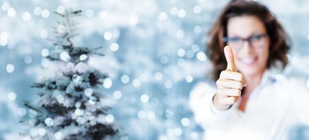 christmas theme, business smiling woman like hand with thumb up on blurred bright lights background.の写真素材