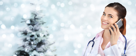 christmas smiling doctor with smart phone on blurred. lights with tree.の写真素材