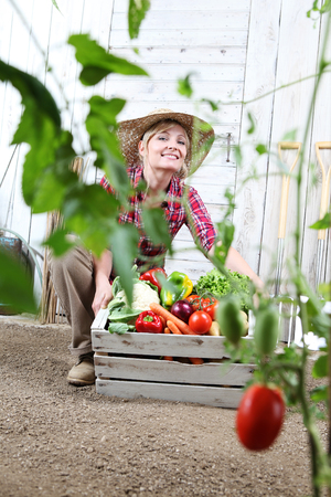 smiling woman in vegetable garden with wooden box full of vegetables.の写真素材