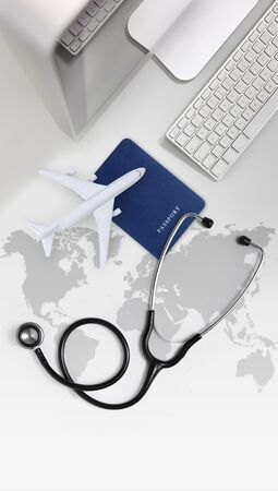 international medical travel insurance concept, stethoscope, passport, computer and airplane on desk office with global map.の写真素材