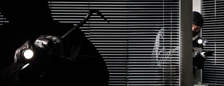 robber burglar thieves are breaking into the house, with torch, crowbar and gun isolated on black door window.の写真素材