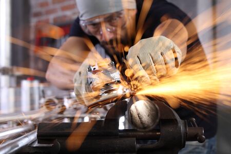 man work in home workshop garage with angle grinder, goggles and construction gloves, sanding metal...