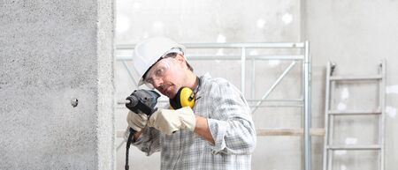 man using an electric pneumatic drill making a hole in wall, professional construction worker with...