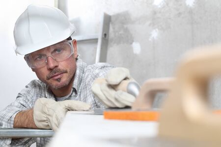 man work, professional construction worker with plastering tools on scaffolding, safety hard hat,...