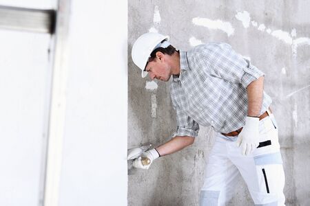 plasterer man at work with trowel plastering the wall of interior construction site wear helmet and protective gloves.の写真素材