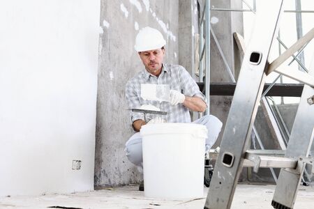 plasterer man at work, take the mortar from the bucket to plastering the wall of interior...