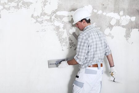 plasterer man at work with trowel plastering the wall of interior construction site wear helmet and protective gloves, isolated and copy space on white wall.の写真素材