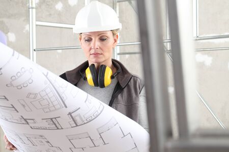 woman construction worker builder looking at bluprint, wearing helmet and hearing protection...