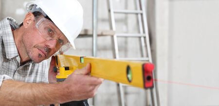 construction man worker measure with level laser wear hard hat and protective glasses  at interior building siteの写真素材