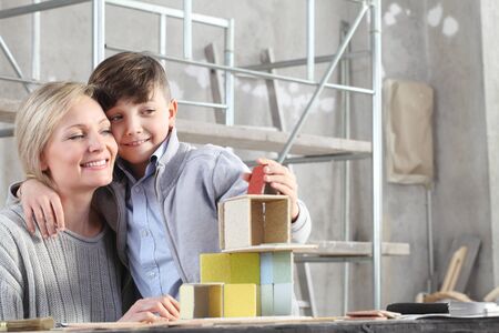 Happy mother and son playing building a house with construction models at interior site. House buy and building goal concept.の写真素材