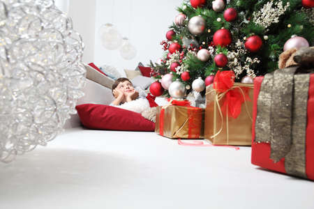 child and the Christmas tree decorated with balls, in the living room lying on the floor next to the wrapped giftsの写真素材