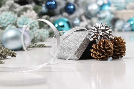merry christmas background, silver gift present box with bow and ribbon, next to blue Christmas balls and pine cones, useful as a greeting card template with copy spaceの写真素材