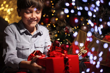 merry christmas, happy child with gift package near the illuminated and decorated tree