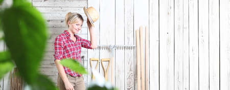 smiling woman in vegetable garden isolated on white wooden shed background with gardening tools, useful as advertising poster or banner template with copy spaceの写真素材