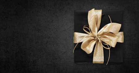 Black Friday gift package wrapped with golden ribbon bow isolated on black background, template for promotional card with copy spaceの写真素材