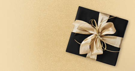 Black Friday gift package wrapped with golden ribbon bow isolated on golden background, template for...