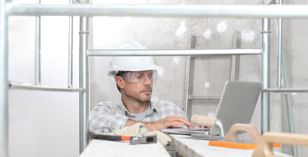 man work, professional construction worker with computer, plastering tools on scaffolding, safety...