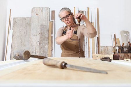 wood crafts, woman artisan carpenter works wood with old manual tools in her workshop, restoration,...