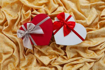 Valentine day, red heart shaped packaging with ribbon bow isolated on damask golden fabric. Useful...