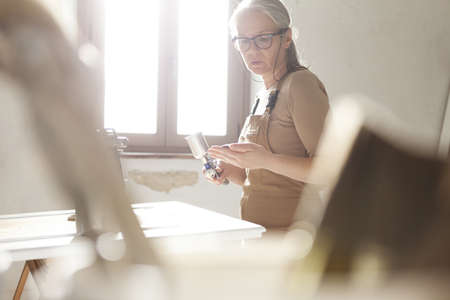 wood crafts, woman artisan carpenter painting with spray gun in her workshop, restoration, diy and handmade works conceptの写真素材