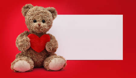 gift card, funny teddy bear with red heart isolated on red background, white sign template with copy spaceの写真素材