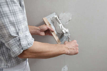 closeup hands man drywall worker or plasterer putting stucco on plasterboard wall using a trowel and a spatula, fill the screw holesの写真素材