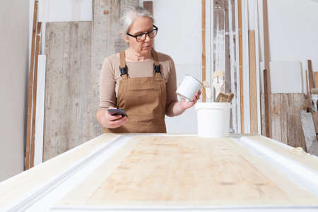 wood crafts, woman artisan carpenter with mobile phone search the internet in her workshop, restoration, diy and handmade works conceptの写真素材